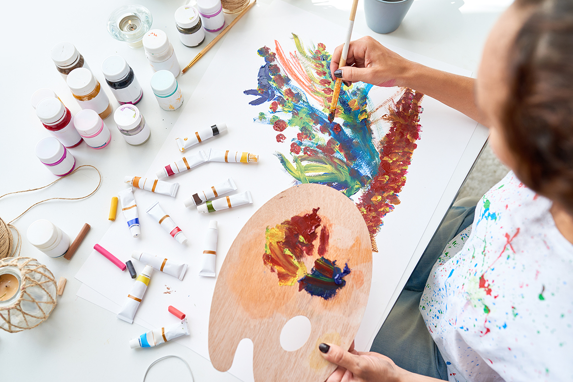 High angle of young woman painting picture with beautiful flowers using oil paints