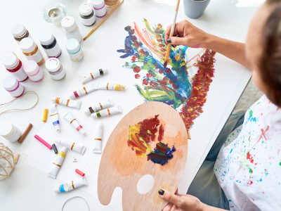 High angle of young woman painting picture with beautiful flowers using oil paints