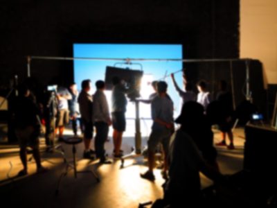 Blurry images of making video production shooting studio in silhouette which have professional equipment such as camera, tripod and blue screen backdrop set for chroma key technique in post process
